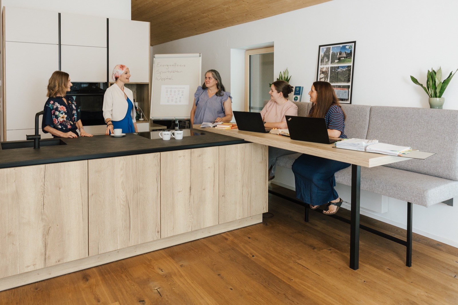 Gemeinschaftsküche der Ideenkuchl: fünf Personen stehen und sitzen im Gespräch an Küchentheke und Sitzbank mit Laptops